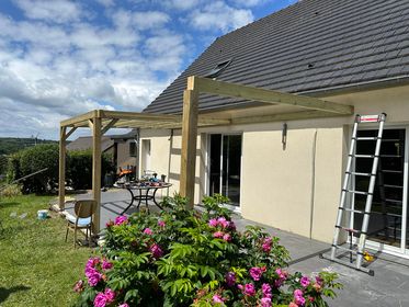 Pergola en bois adossée à une maison avec une terrasse et un jardin fleuri.