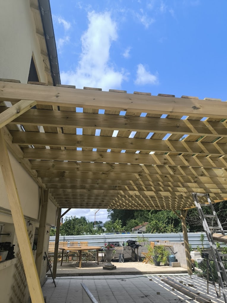 Pergola en bois brut installée sur une terrasse pavée avec mobilier de jardin visible