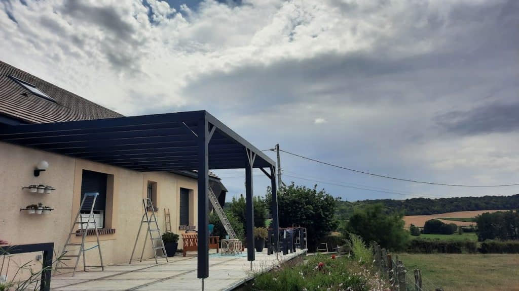Pergola bois sombre adossée à une maison avec vue sur la campagne